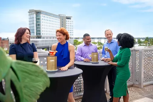 Group on rooftop enjoying drinks at hightop table overlooking Luminary hotel in downtown Fort Myers